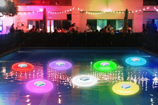 Illuminated floating pool lights in various colors light up a swimming pool during a nighttime outdoor party.