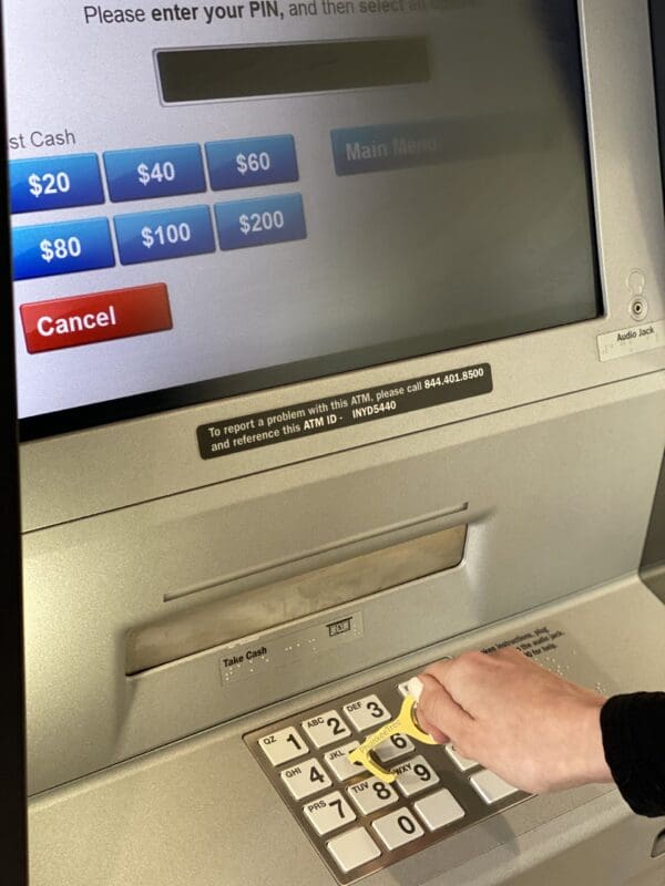 A person using an atm, pressing the number pad, with cash withdrawal options displayed on the screen above.