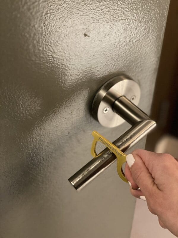 Hand using a yellow "police line do not cross" barricade tape to secure a door handle.