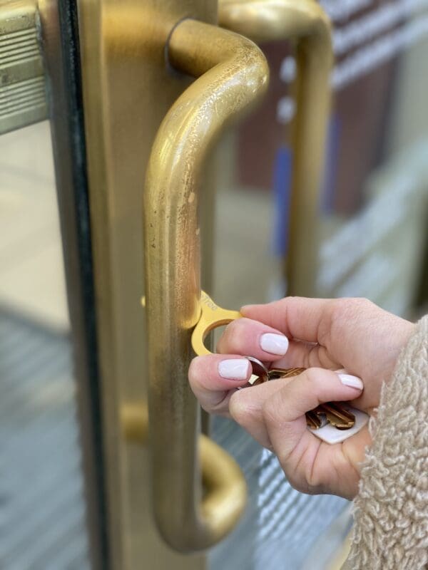 A person using a brass key-shaped tool to open a door without directly touching the handle.