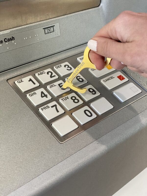 A hand using a yellow key-shaped tool to press the number 6 on an atm keypad.