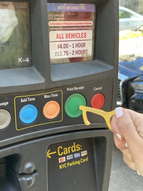 A hand inserts a yellow nyc parking card into a parking meter displaying payment options and fees on its screen.