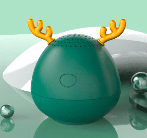 A green, egg-shaped speaker with orange deer antlers on a light green background, surrounded by small glossy spheres and a white object.