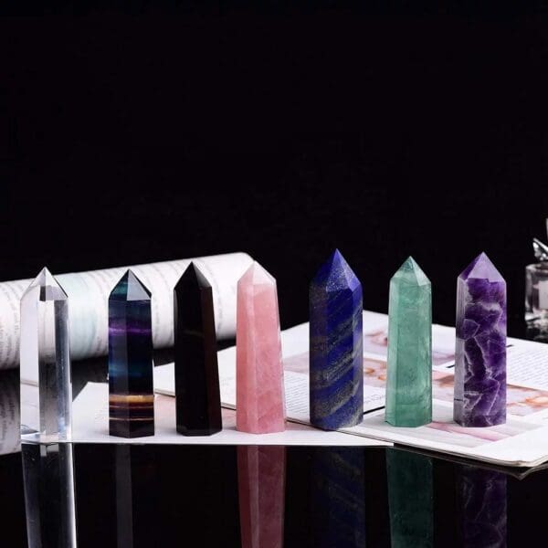 A collection of six colorful, polished crystal towers of varying hues, neatly arranged on a reflective surface against a dark background.