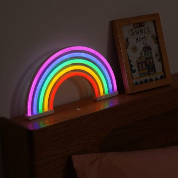 A colorful neon rainbow light sits on a wooden headboard next to a framed picture with the text "sweet home.