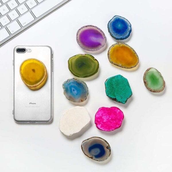 Silver iphone surrounded by colorful agate slices on a white surface, with a keyboard partially visible in the top left corner.