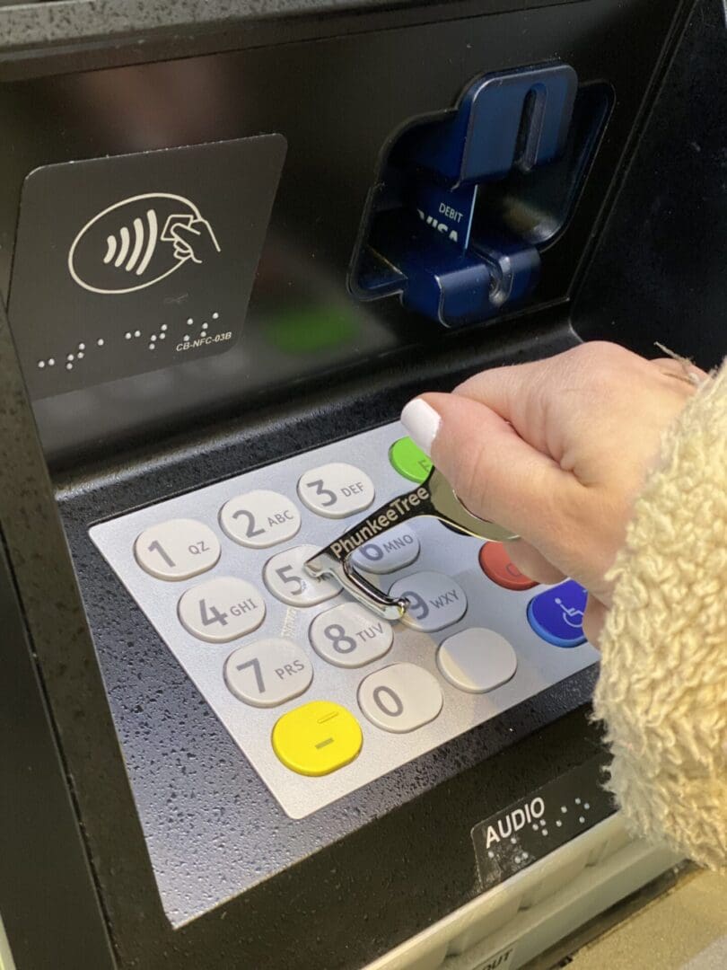 A person's hand entering a pin on an atm keypad, featuring braille and an audio function for accessibility.