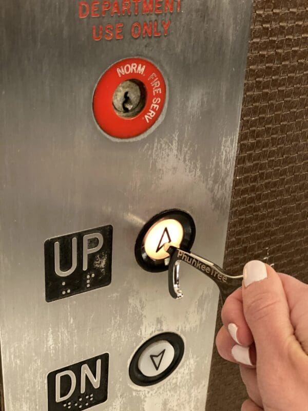 A hand inserting a key labeled "phunketree" into an elevator control panel with buttons labeled "up" and "down" and a red "norm pres" button.