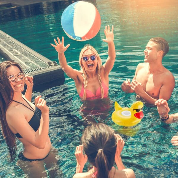 Young adults enjoying a sunny day in a pool, with a woman catching a beach ball and others smiling around her.