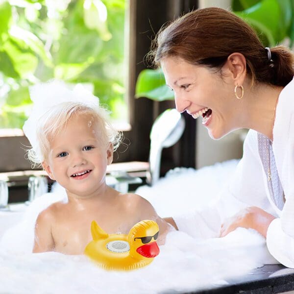 A joyful woman and a young child with bubbles around in a bath, smiling and playing, the child wearing a yellow duck floatie.