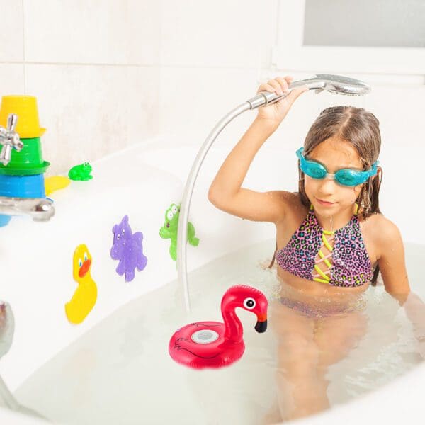 Young girl wearing goggles and a swimsuit playing with a shower head and rubber toys in a bathtub.