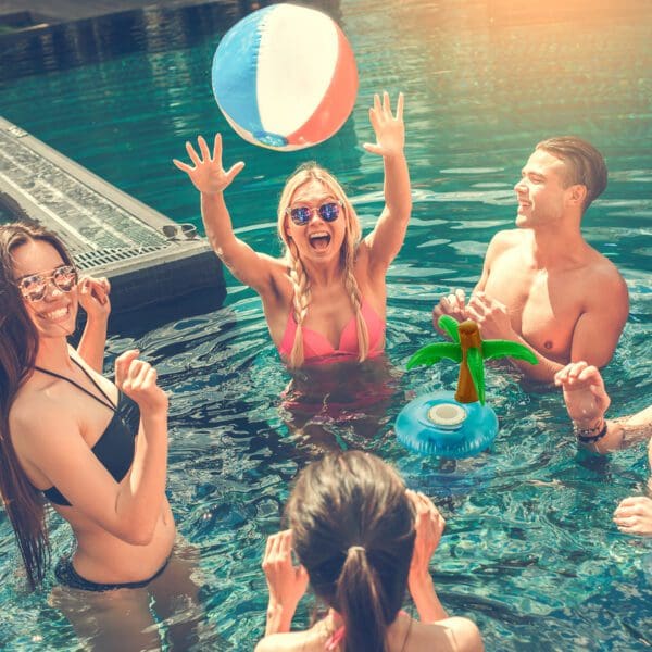 Young adults enjoying a sunny day in a pool with a beach ball and inflatable drink holders.