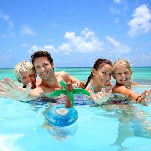 A family of four, including two adults and two children, joyfully posing in clear, shallow ocean water under a bright sky.