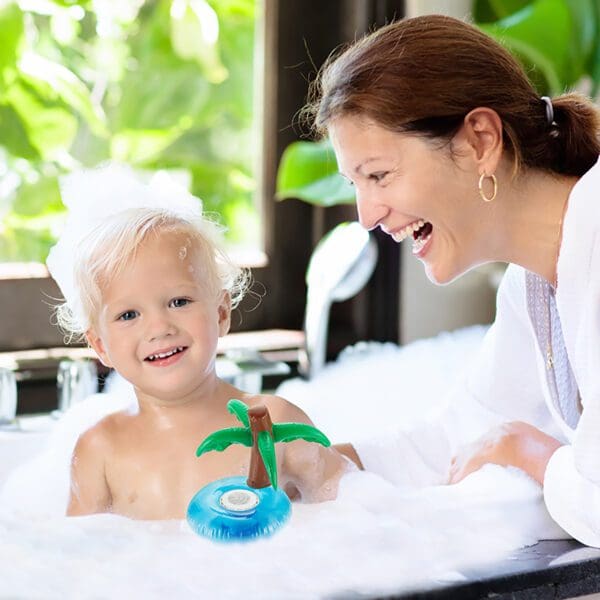 A smiling woman and a young child enjoying a bubble bath with a toy palm tree.
