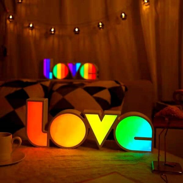 Illuminated 'love' signs in vibrant colors on a table inside a cozy room with warm lighting and hanging fairy lights.