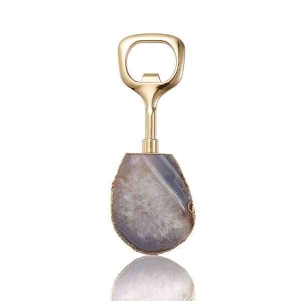 Gold bottle opener with an agate stone handle, displayed against a reflective white surface.