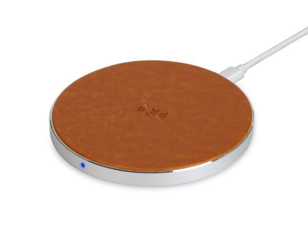 Wireless charging pad with a brown leather top and metallic edge, connected to a white cable, on a white background.