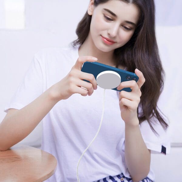 A woman in a white t-shirt playing a video game using a blue handheld gaming console while sitting at a wooden table.