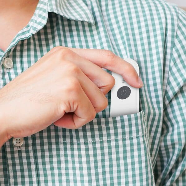 A person using a portable white device with a power button symbol on it, pressing it against their green and white checked shirt.