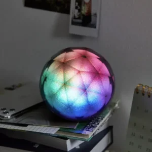 A colorful LED Crystal Ball Wireless Speaker on a stack of books beside a calendar and wall with photos and notes.