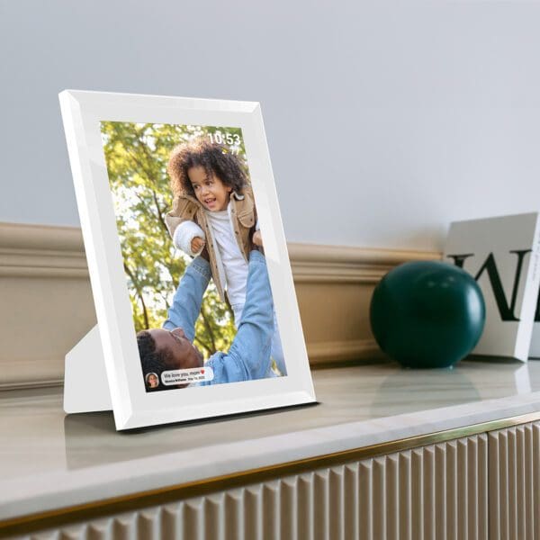 A Digital Picture & Video Frame displaying an image of a young child riding on a man's shoulders in a park, placed on a shelf next to decorative items.