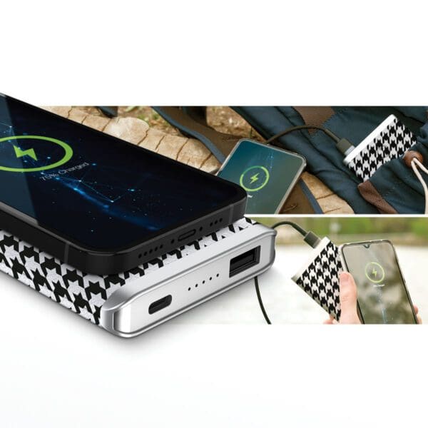 A Grey - Leather 5K Wireless Charging Power Bank with houndstooth design charging multiple smartphones, one via cable and another wirelessly, placed on a wooden surface next to a backpack.