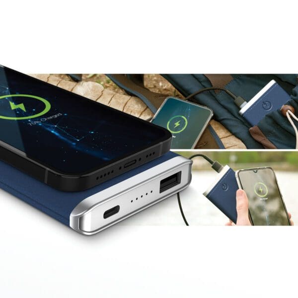 Portable Grey - Leather 5K Wireless Charging Power Bank charging two smartphones, displayed on a table alongside a backpack and a notebook.