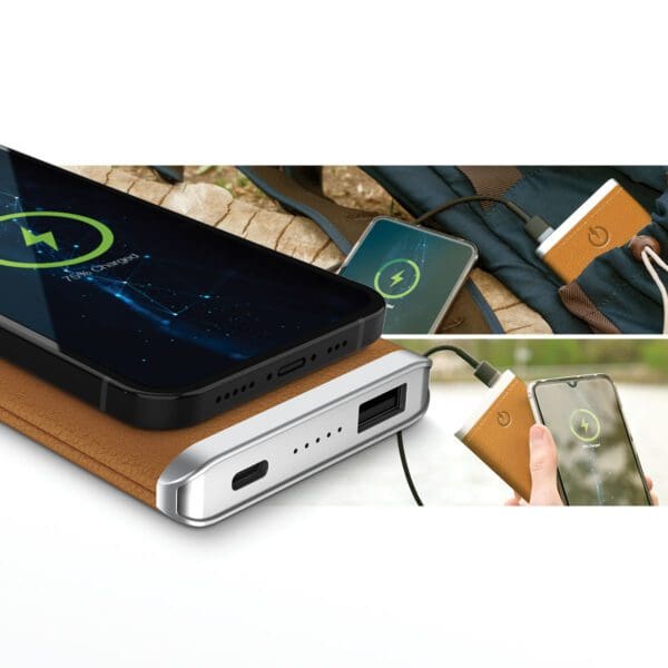 Three smartphones charging via a Grey - Leather 5K Wireless Charging Power Bank, placed on a table next to a backpack.