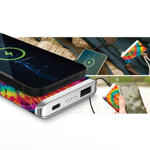 Portable Grey - Leather 5K Wireless Charging Power Bank charging two smartphones on a colorful fabric surface, with one phone connected via cable and the other using wireless charging.